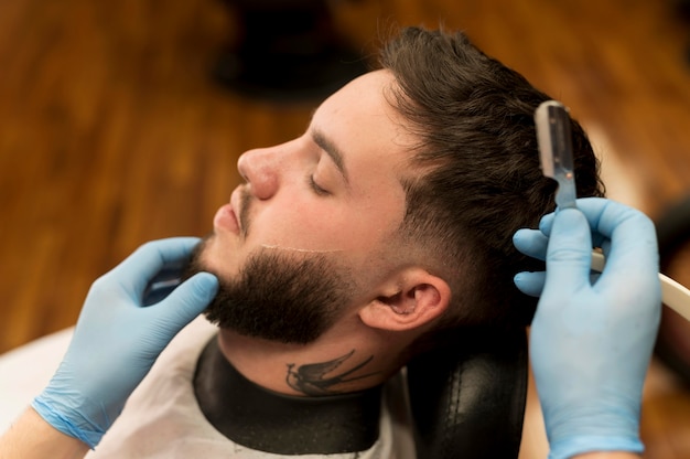 Barber shaving and contouring male customer's beard