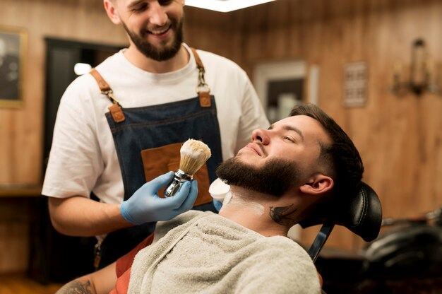 Barber using shaving cream to contour male customer's beard