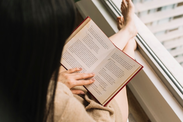 Barefoot female reading near window