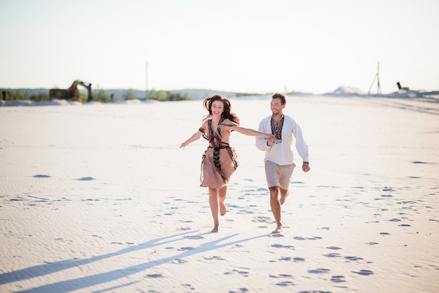 Free photo barefooted couple in bright embroidered clothing runs on a white sand