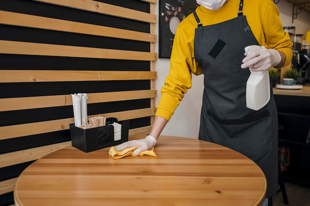 Barista cleaning table while wearing medical mask