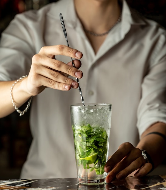 Bartender mixes mojito cocktail with metal spoon