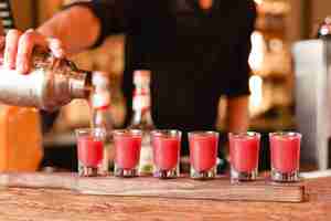 Free photo bartender putting red cocktails into small glasses from cocktail shaker.