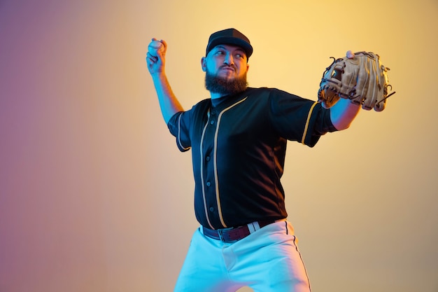 Baseball player, pitcher in a black uniform practicing and training on gradient background in neon light.