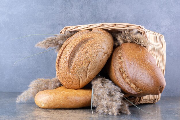 Basket filled with bread loaves and feather grass stalks on marble surface