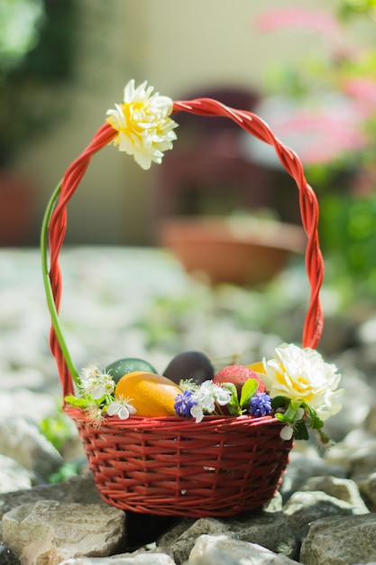 Free photo basket filled with colorful easter eggs and decorated with white flowers on the rocks