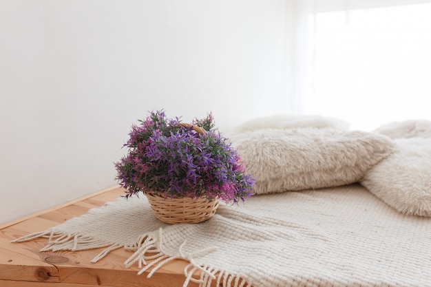 Free Photo basket of jute with purple flowers wooden floor with knitted pillows and covering