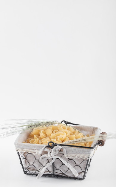 Basket of raw pasta with ear of wheat on white.