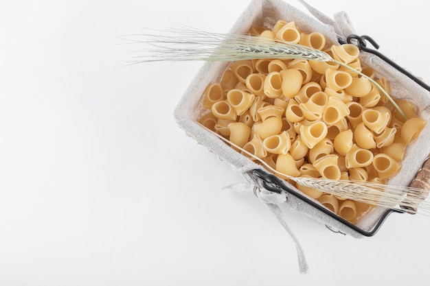 Free photo basket of raw pasta with ears of wheat on white.