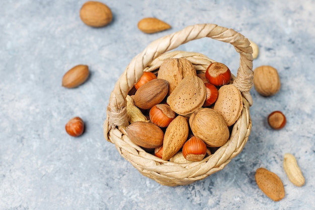 Basket reach in various kinds of nuts in shells, peanuts, almonds, hazelnuts and walnuts on concrete surface