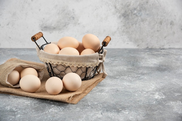 Basket and sackcloth of organic fresh uncooked eggs on marble surface.