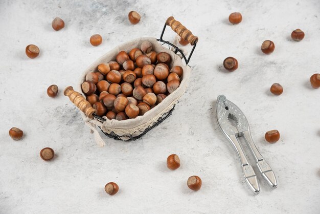 Basket of shelled hazelnuts and nut cracking tool on marble table. 