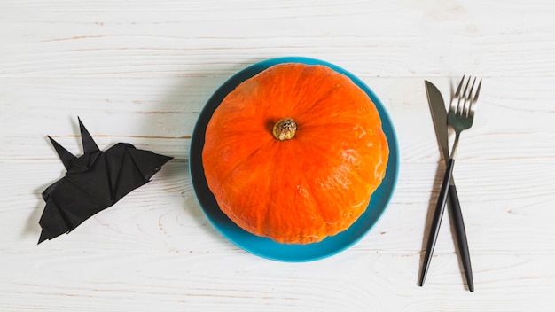 Bat origami and pumpkin in dish standing on wooden desk