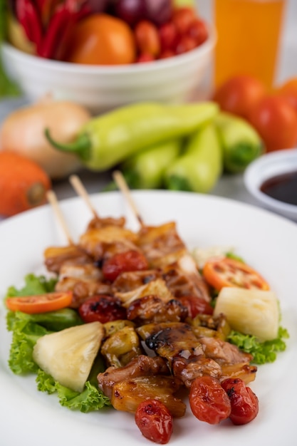 BBQ with a variety of meats, complete with tomatoes and bell peppers on a white plate.