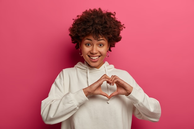 Free photo be my valentine. pleasant looking curly woman expresses love, makes heart gesture, has romantic feelings