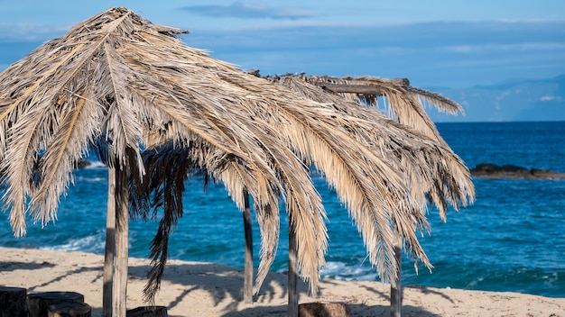 Beach of the Aegean sea with umbrellas made of palm branches, in Greece