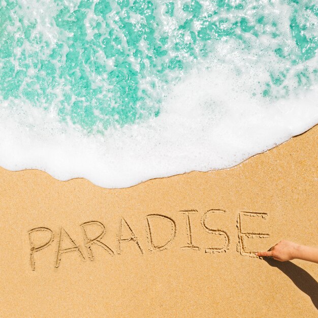 Beach concept with paradise written in sand