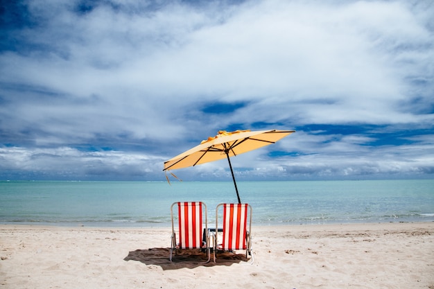 Beach parasol and red beach chairs on a shore