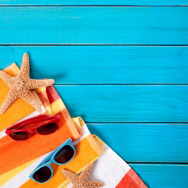 Beach scene with orange striped towel, starfish and sunglasses on old blue painted wood decking.  Space for copy.