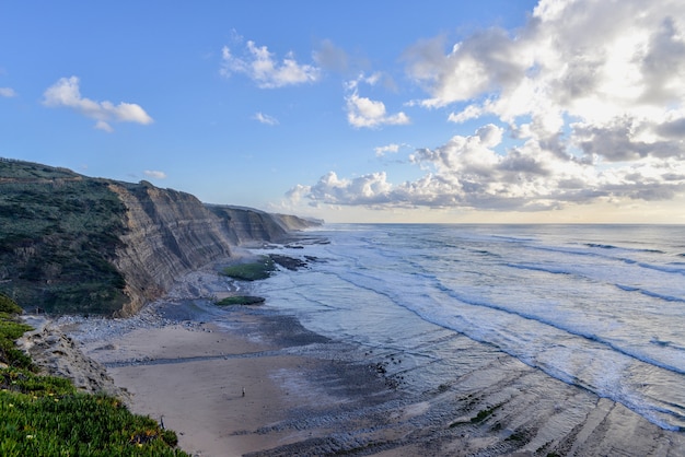 Beach surrounded by rocks and the sea under a cloudy sky during the sunrise