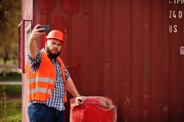 Free Photo beard worker man suit construction worker in safety orange helmet near red barrel makes selfie on phone