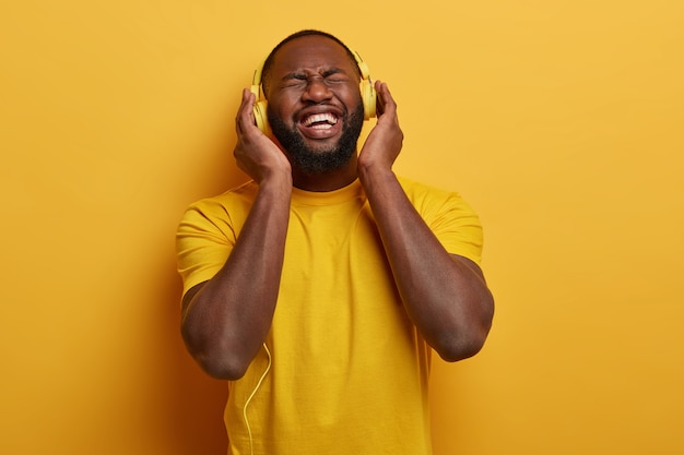 bearded black man fascinated with nice quality of headphones, listens pleasant music, connected to some electronic device