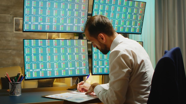 Free photo bearded businessman taking notes while checking stock market from home office.