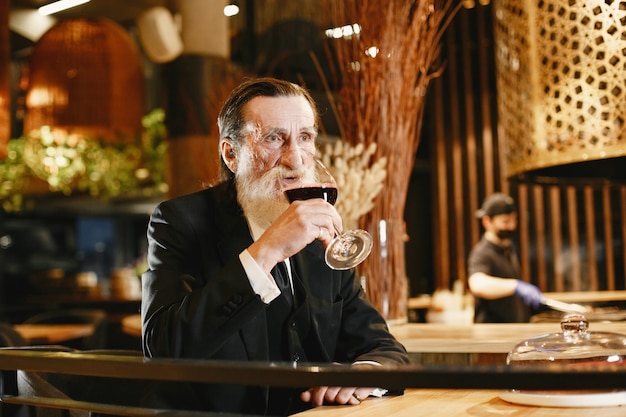 Bearded elderly businessman. Man in a restaurant. Senior in black suit.