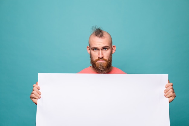 Free photo bearded european man in casual peach isolated, holding white empty paper board with sad unhappy face