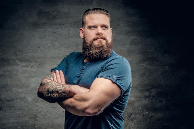 Bearded fat male with tattoo on arms posing over grey background.