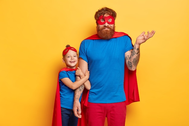 Free photo bearded ginger father looks confusingly, raises tattooed arm