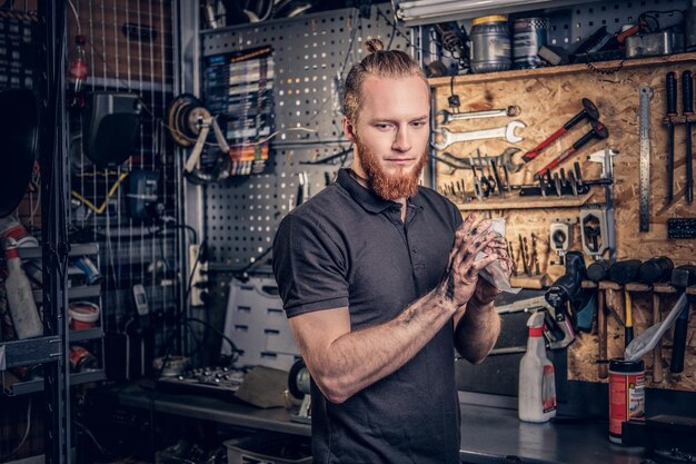 Bearded male bicycle mechanic cleans his arms after bike service manual in a workshop.