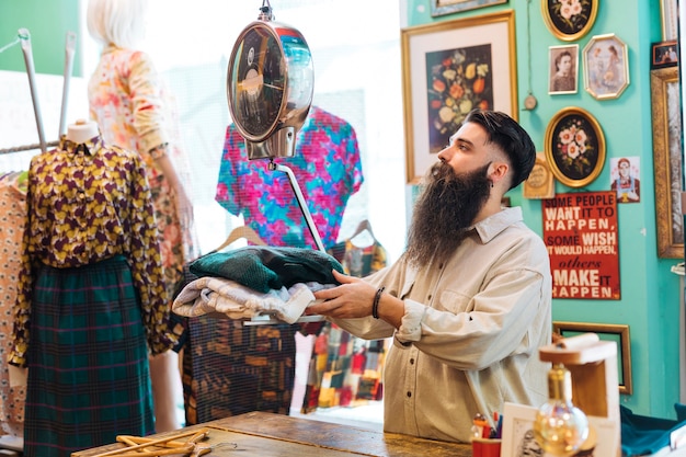 Free photo bearded male owner checking fabric weight on scales at his clothing shop