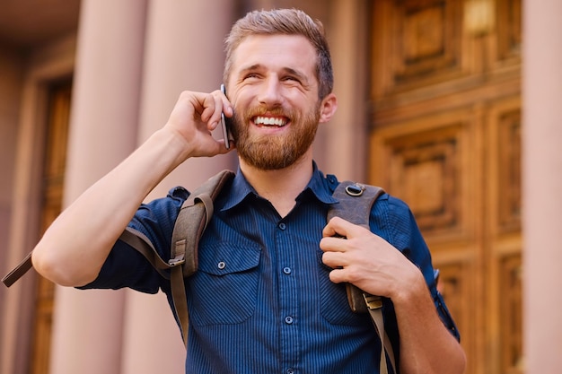 Bearded male with backpack speaking by smart phone in an old European town.