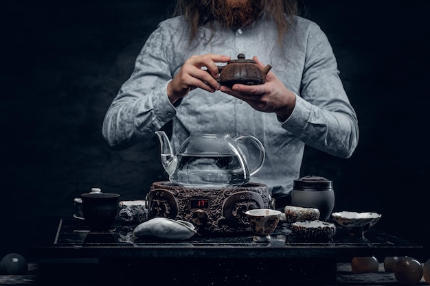 Free photo bearded male with long hair preparing tea in asian style.