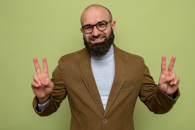 Free Photo bearded man in brown suit wearing glasses looking smiling cheerfully showing v-sign