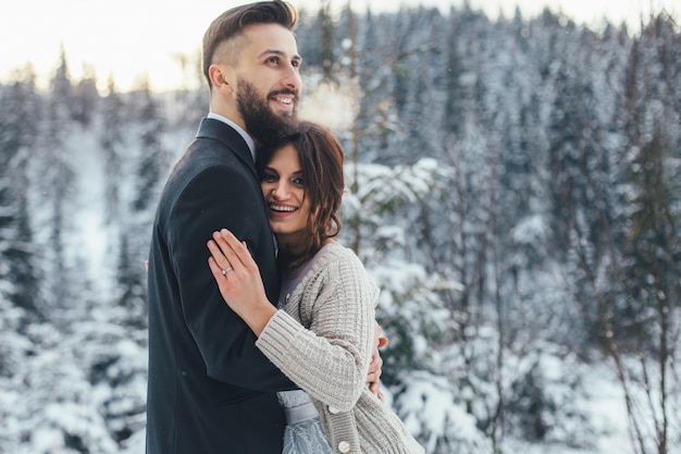 Bearded man and his lovely bride pose on the snow in a magic winter forest