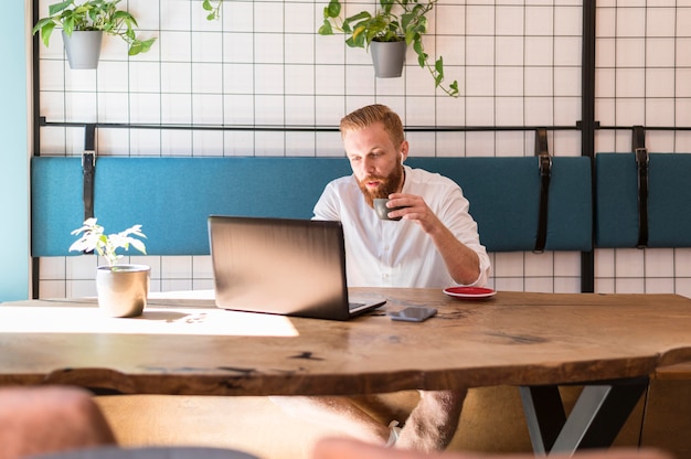 Free photo bearded man holding a cup of coffee while working