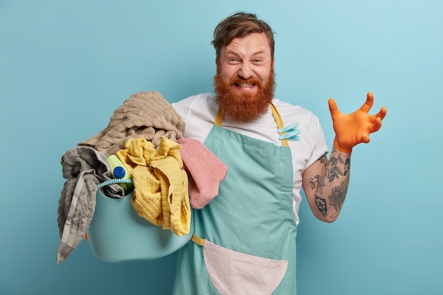 Bearded man holds laundry basket, overwhelmed by household chores