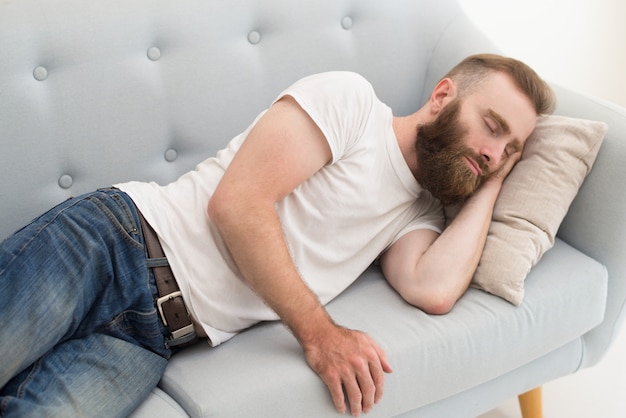 Bearded man lying and dosing on sofa