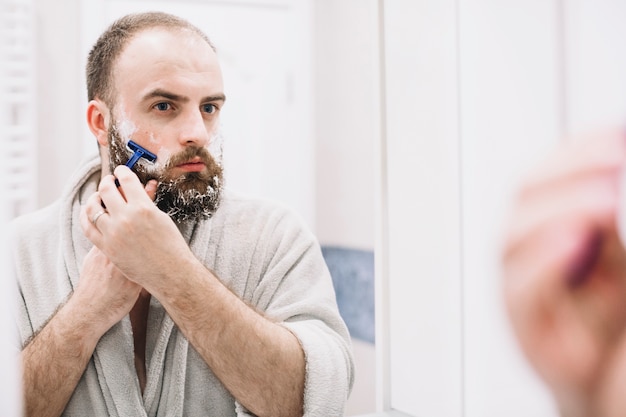 Free photo bearded man shaving in front of mirror