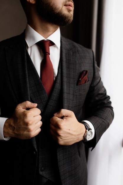 Bearded man in stylish tuxedo and red tie, strong man's hands