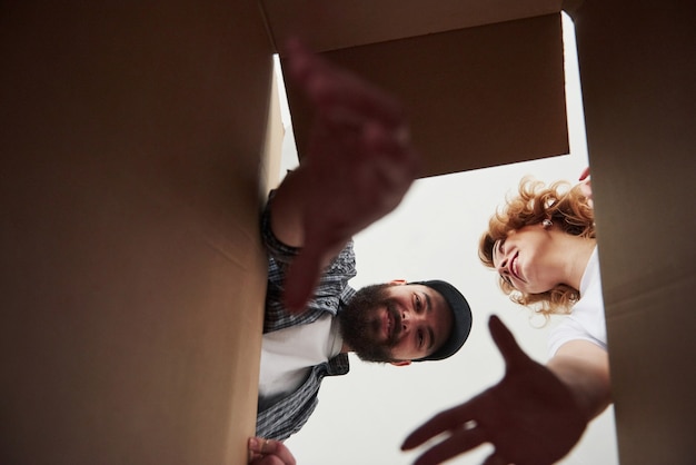 Free photo bearded man trying to reach the item down of a box. happy couple together in their new house. conception of moving