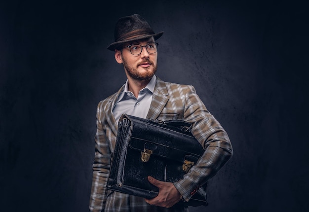 A bearded man wearing casual suit in a hat and glasses holds sui