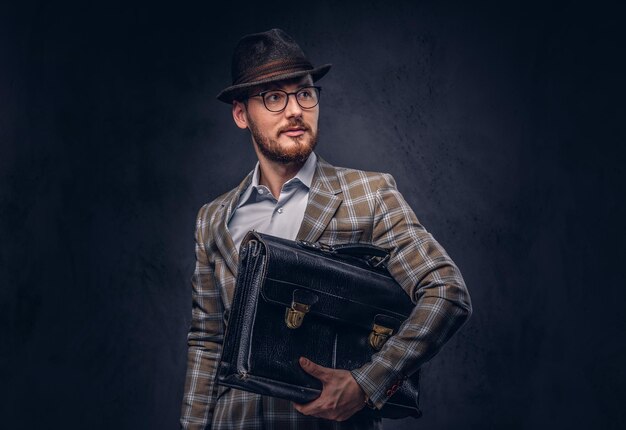 A bearded man wearing casual suit in a hat and glasses holds sui