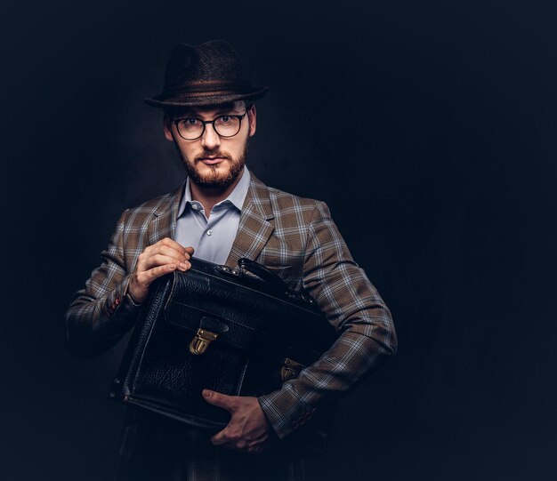 A bearded man wearing casual suit in a hat and glasses holds sui