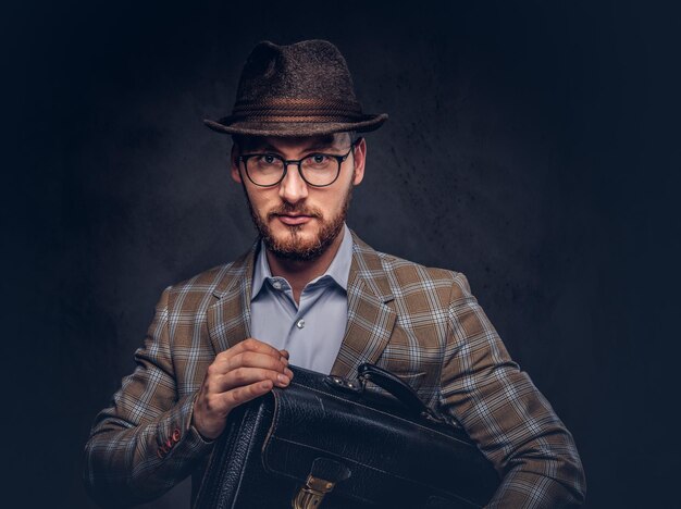 A bearded man wearing casual suit in a hat and glasses holds sui