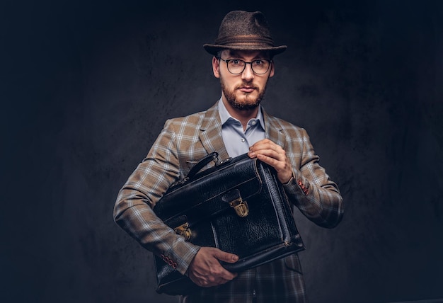 A bearded man wearing casual suit in a hat and glasses holds sui