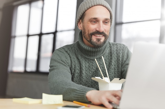 Bearded man wearing knitted warm sweater and hat having lunch