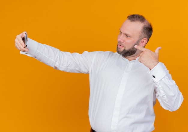 Bearded man wearing white shirt doing selfie smiling standing over orange wall